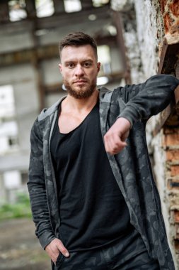 Yakışıklı bir maçonun portresi, yıkık dökük binanın arkasında duruyor. Modern erkekte moda giysileri..