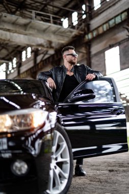 Yakışıklı manken adam lüks arabanın kapısını açmış. Koyu renk arabanın yanında siyah bir adam vardı..