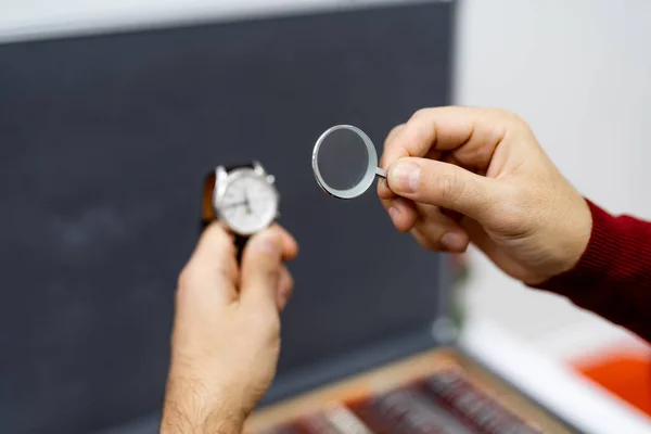 Unrecognizible man looking at hand watches through magnifying glass. Vintage watches and loupe.