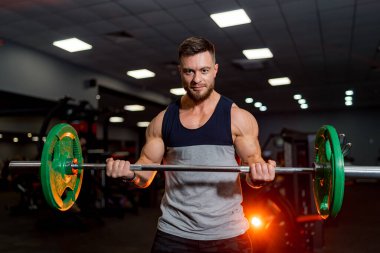 Halterle egzersiz yapan formda kaslı bir adam. Kaslı genç adam karanlık spor salonunda ağırlık kaldırıyor. Yakın çekim..