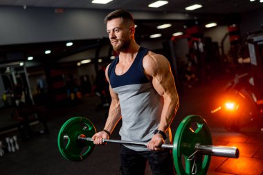 Halterli güçlü bir vücut geliştirici. Beden dersinde fotoğraf çekimi. Kapalı alan spor konsepti. Kasları poz vermek ve pompalamak.