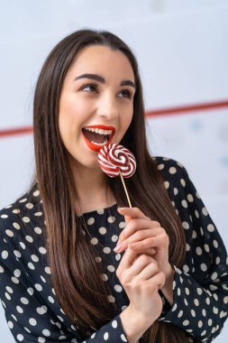 Elinde lolipop olan noktalı tişörtlü genç bir kız. Beyaz arka planda şekerleri olan neşeli bir bayan..