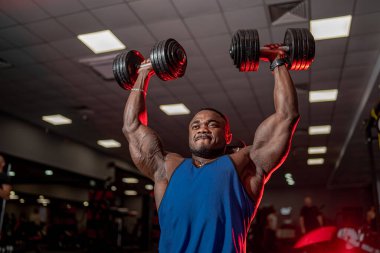 Afrika kökenli Amerikalı sporcu, kafasının üzerinden dambıl pompalıyor. Mükemmel kasları olan güçlü vücut geliştiricilere aşağıdan seçici odaklanma.