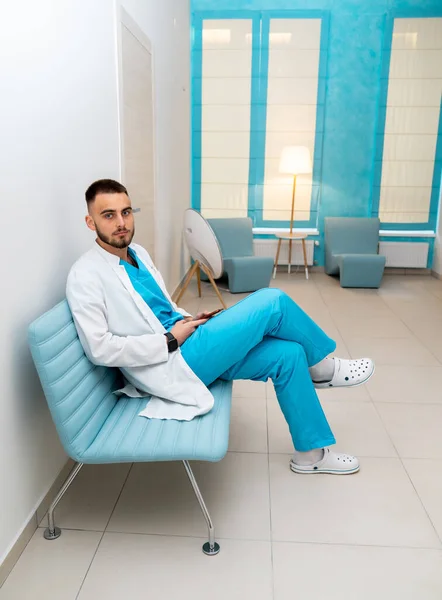 Προσεκτικός Νεαρός Άνδρας Γιατρός Ποδιά Κάθεται Στον Καναπέ Στο Διάδρομο — Φωτογραφία Αρχείου