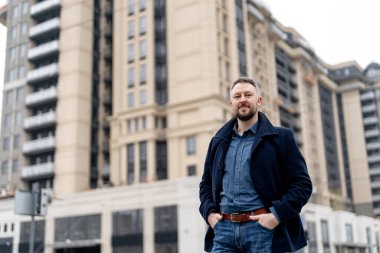 Sokakta elleri ceplerinde duran resmi elbiseli bir adam. Moda ve şık yakışıklı genç erkek. Arka planda modern bina.