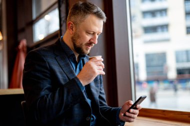 Kafedeki dalgın bir iş adamının otantik görüntüsü. Koyu takım elbiseli bir iş adamı internette sörf yapıyor..