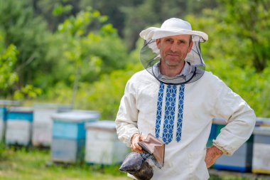 Arı kovanında çok çalışan bir arıcı kameraya poz veriyor. Elinde arı içicisi olan adam. Apiculture kavramı.