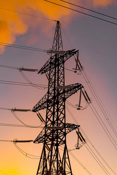 Metal electric pillar with orange sky background. Power transmission facilities. High voltage pylons against sunset background. Energy and industrialization concept. Selective focus