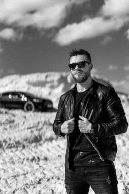 Lüks araba geçmişi olan vahşi bir adam yolda duruyor. Siyah beyaz fotoğraf.