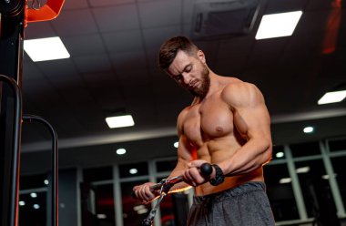 Atletik vücut. Gömleksiz manken adam kameraya spor aletleriyle poz veriyor. Mükemmel vücudu olan güçlü kaslı bir adam. Yakın çekim..