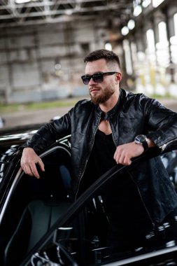 Başarılı, modaya uygun, sakallı, zengin bir adam pahalı bir arabaya biniyor. Arabanın yanındaki sakallı adam. Deri ceketli maço bir erkek. Yakın çekim..