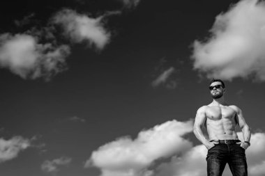 Mükemmel vücutlu bir adam gömleksiz kaslarını şişiriyor. Gökyüzü bulutlu. Siyah beyaz fotoğraf kavramı.