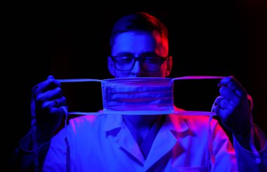 Doktor cerrahi maskeyi yüze yakın tutuyor. Stüdyoda siyah geçmişi olan koruyucu önlüklü bir doktor. 