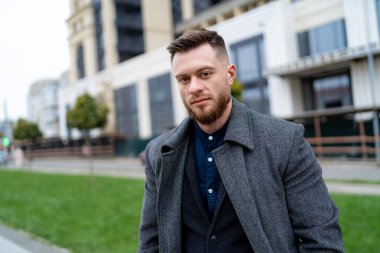 Resmi kıyafetler giymiş yakışıklı ve neşeli genç bir iş adamı. Ceketli bir erkek şehir manzaralı kameraya bakıyor..