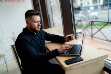 Bir fincan kahveyle rahat bir kafede oturup çalışan mutlu bir işadamı..