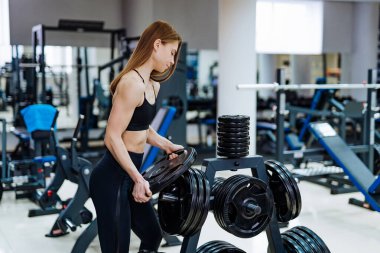 Güzel sarışın kadın ısınıyor ve spor salonunda egzersiz yapıyor. Koyu renkli sporlarda kadınlar spor malzemelerinin yanında giyerler. Yakın çekim..