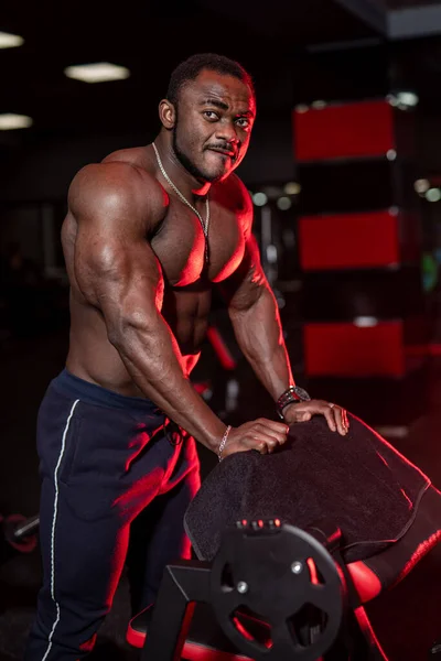 Pumped up shirtless african american sportsman in modern gym with up to date sport equipment. Cute black man under dramatic red law key lightning. Closeup.