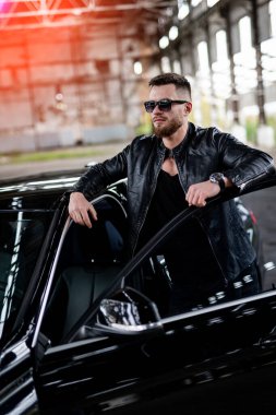 Siyah ceketli adam arabanın kapısının yanında duruyor. Moda araba ve sürücünün portresi..