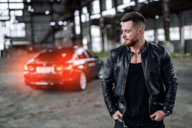 Yetişkin stili bir adam modern bir arabanın önünde dikilip izliyor. Siyah renklerin kombinasyonu.