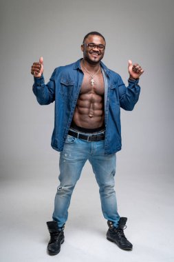 Neşeli Afro-Amerikan adam ayakta duruyor. Yetişkin adam parmakları havada poz veriyor. Koyu mavi gömlekli ve kotlu yarı çıplak çekici bir erkek..