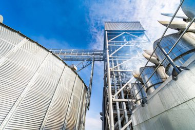 Tahıl deposu için aşağıdaki büyük tankın tepesinde özel olarak inşa edilmiş metal bir köprü var. Mavi gökyüzü parçalı kırpılmış fotoğraf.