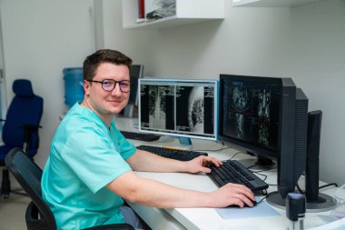 Roentgenolog erkek röntgen resimli monitörlerin yanında otururken kameraya bakıyor. Radyolog, travmatolog ya da sağlık sigortası konsepti. Yakın çekim..