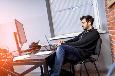 Gündelik giysiler içinde yakışıklı genç bir adam ofiste çalışıyor. Çevrimiçi çalışan kendine güvenen serbest erkek.