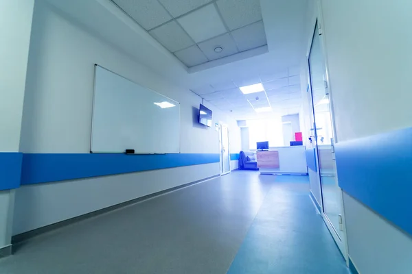 Wide light hall in modern hospital. White and blue colors. Nurse station and whiteboard.