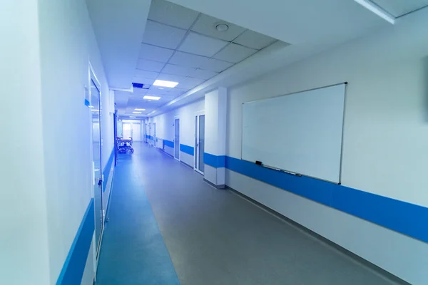 Long hospital hall in light white and blue colors. Many doors and whiteboard on wall.