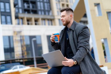 Genç başarılı iş adamı sokakta kahve molası verdi. Bilgisayarla çalışan yakışıklı bir adam..