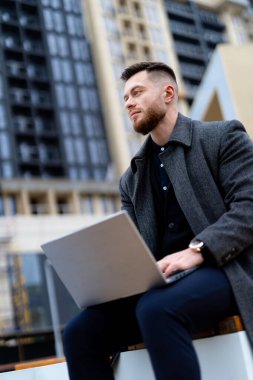 Düşünceli adam başka tarafa bakıyor. Modern sokakta dizüstü bilgisayarla çalışan yetişkin bir işadamı..
