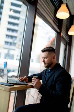 Modern kafede dizüstü bilgisayarla çalışan yakışıklı bir genç. Not defteriyle çalışan şık bir erkek..