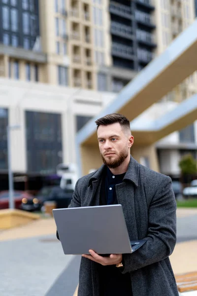 Uporczywy Biznesmen Szarym Luźnym Płaszczu Pracujący Laptopie Nowoczesna Szeroka Ulica — Zdjęcie stockowe