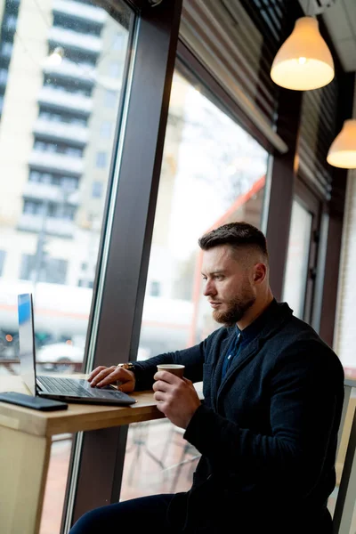 Modern kafede dizüstü bilgisayarla çalışan yakışıklı bir genç. Not defteriyle çalışan şık bir erkek..
