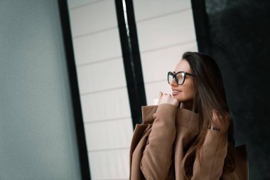 Gözlüklü, kahverengi paltolu şık bir kızın moda portresi. Örnek kız için seçici bir odak noktası. Yakın çekim..