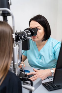 Kadın göz doktoru, tretment reçetesi için hastanın gözlerindeki özel ekipmanlara bakar. Yakın çekim..