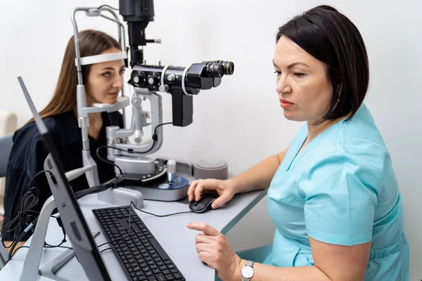 Deneyimli kadın doktor göz doktoru modern klinikteki genç bayanın görüşünü kontrol ediyor. Göz hekimliği kliniğinde doktor ve hasta..