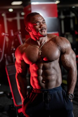 Çağdaş spor salonunda dikilip başka tarafa bakan güçlü yarı çıplak Afrikalı Amerikalı vücut geliştirici..