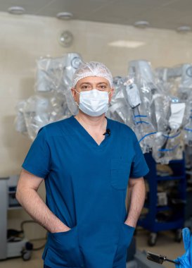 Ameliyathanede kameraya bakan erkek cerrahın portresi. Modern hastane ameliyathanesinde önlüklü ve tıbbi maskeli bir doktor..