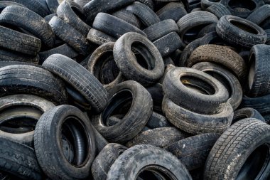 Eski bir fabrikada ışık sızıntısı olan kullanılmış lastiklerin arka planında duran geniş lastik tekerlek. Eski, yıpranmış lastikler terkedilmiş bir çöplükte