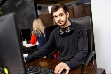 Web sitesi tasarım programlama ve kodlama teknolojileri. Bilgisayarın yanında oturan bir adam kameraya bakıyor. Yaratıcı ofis kavramı