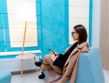 Kanepede oturan genç ve güzel bir kadın. Gözlüklü güzel bir kadın. Bir kadın telefona bakar. Yakın çekim.