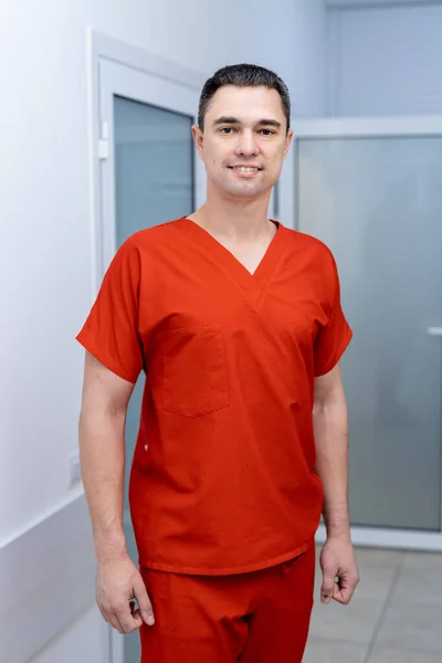 Portrait of male surgeon in hospital hall looking at camera and smiling. Doctor in red clothes in modern hospital. Medicine concept