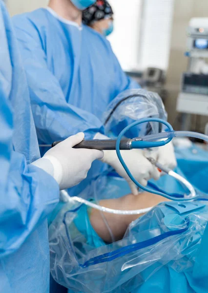 Confident surgeon wearing protective mask holding special equipment and working with his colleagues during the operation at the knee. Medicine concept