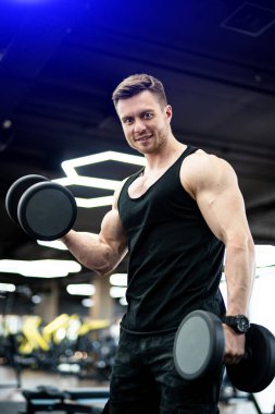 Vücut geliştirici pazılarını çalıştırıyor. Güçlü yakışıklı adam spor salonunda çok çalışıyor..