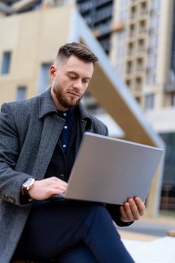 Gri montlu ısrarcı iş adamı dizüstü bilgisayarla iş yapıyor. Arka planda modern geniş cadde. İş konsepti