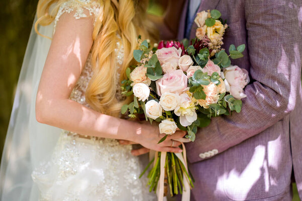 Bride and groom at wedding day walking outdoors. Bridal couple, happy newlywed woman and man concept. Loving wedding closeup with a bouquet