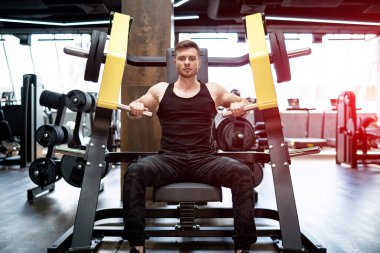 Spor salonunda çalışan yakışıklı bir vücut geliştirici. Kaslı atletik adam sıkı çalışıyor..