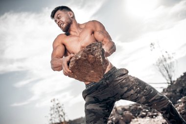 Ağır kayalarla dağda atletik adam antrenmanı. Taş ocağı geçmişi. Açık hava eğitim konsepti. Düşük açı