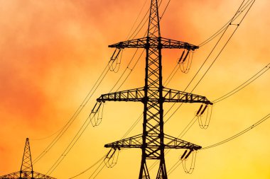 Akşam gökyüzüne karşı iletim hatları. Batan güneşin arka planında kabloları olan yüksek voltajlı elektrik kuleleri. Elektrikli siyah sütunlar